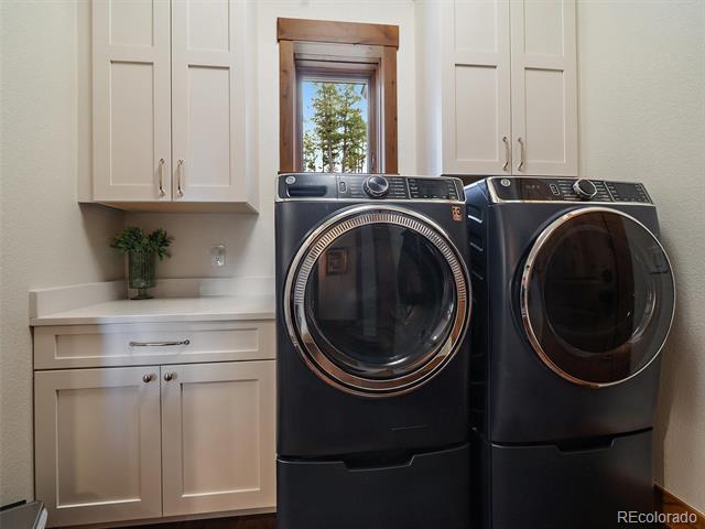 Laundry room with dark front-loading washer and dryer beneath white cabinets, beside a small window.