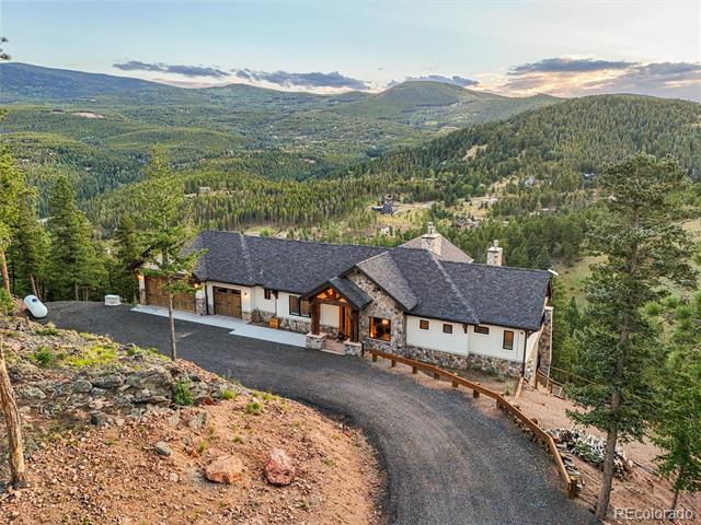 Mountain home with a stone exterior and winding driveway, overlooking forested hills and distant ridges.