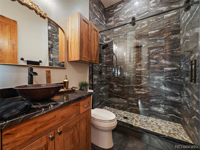 Bathroom with a marble-look walk-in shower and wood vanity with vessel sink.