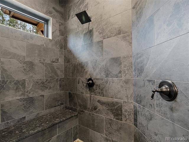 Walk-in shower with gray tile, rainfall showerhead, built-in bench, and a narrow window.