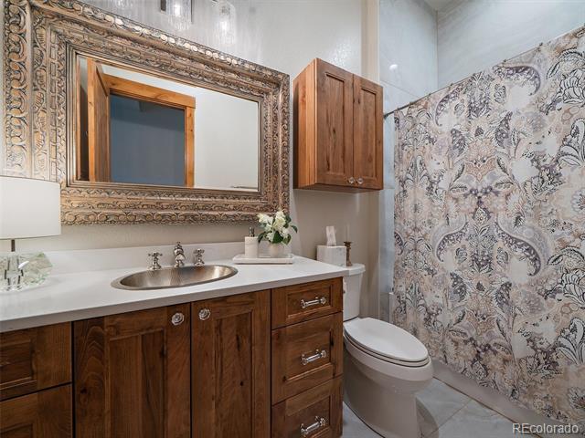 Bathroom with a dark wood vanity, ornate mirror, and patterned shower curtain.