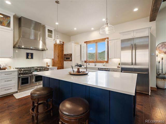 Kitchen with a large navy island, stainless steel appliances, and mountain views through a wood-trimmed window.