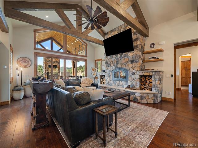 Living room with a stone fireplace, vaulted timber beams, and large windows.