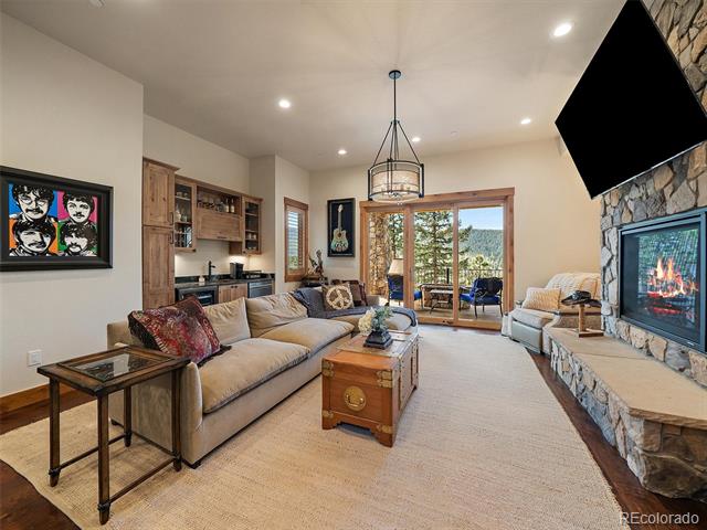 Living room with a beige sectional, stone fireplace, and glass doors opening to a tree-lined view.
