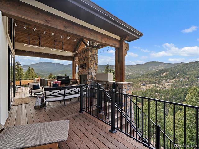 Covered deck with lounge seating and a stone fireplace overlooking a wooded mountain valley.