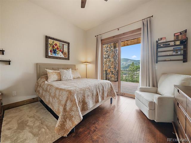 Bedroom with a bed, white armchair, and open balcony doors overlooking mountains.