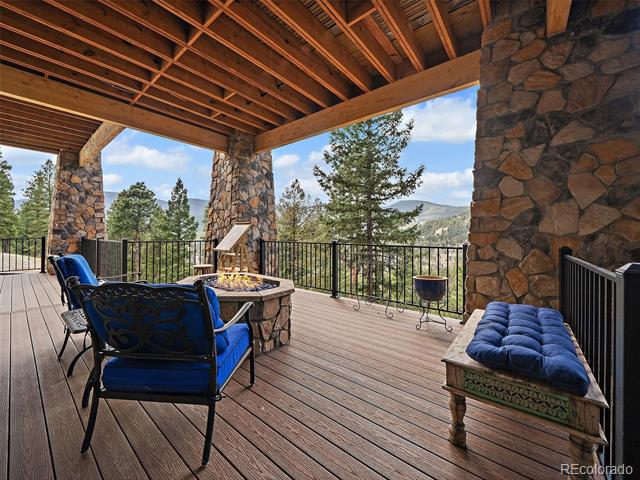 Covered timber deck with stone columns, blue seating, a fire pit, and mountain views.