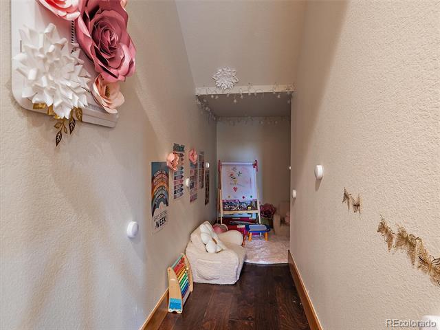 Hallway with dark wood floors, a child-sized chair, colorful books, and oversized paper flowers.