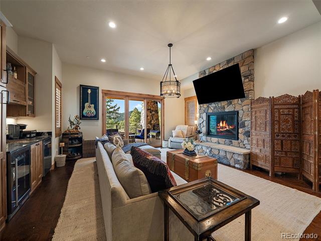 Furnished living room with a stone fireplace, mounted television, and glass doors overlooking trees.