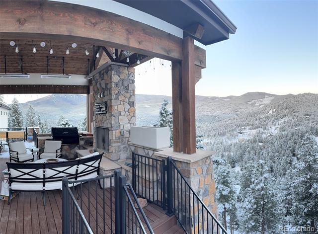 Covered stone-and-timber deck with patio seating overlooking snowy mountains.