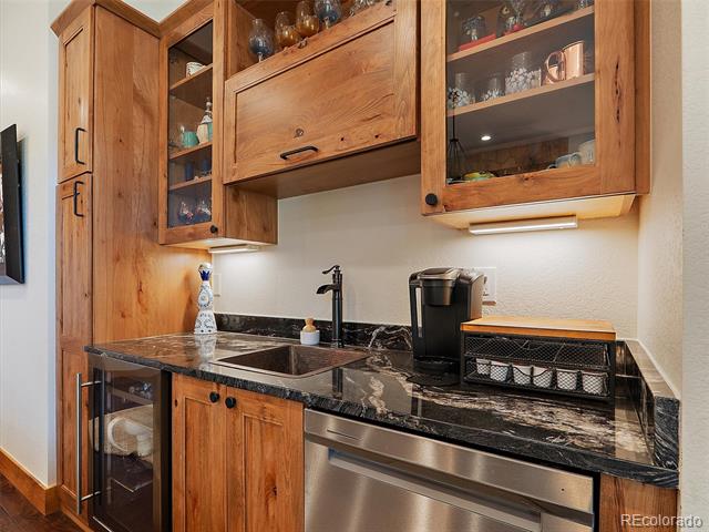 Kitchen wet bar with wood cabinets, black marble counters, a sink, and a glass-front beverage refrigerator.