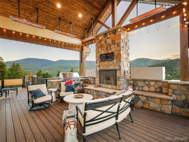 Covered mountain-view patio with lounge seating, a stone fireplace, and an outdoor grill.