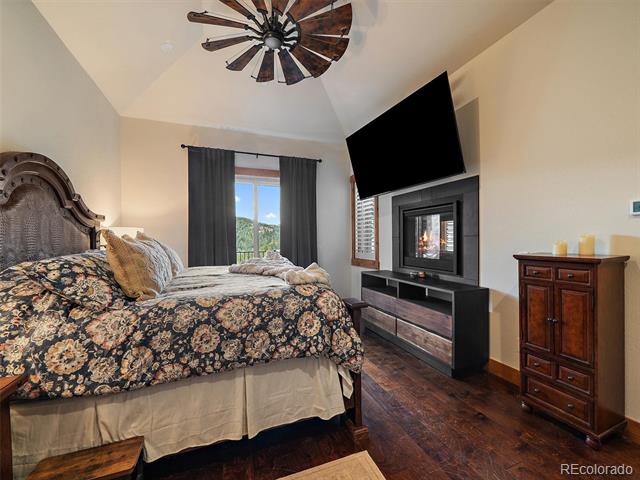Bedroom with a floral bedspread, vaulted ceiling, fireplace, and wooded mountain view.