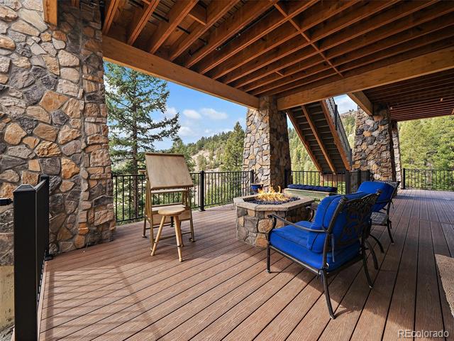 Covered deck with a fire pit and blue chairs overlooking pine-covered mountain slopes.