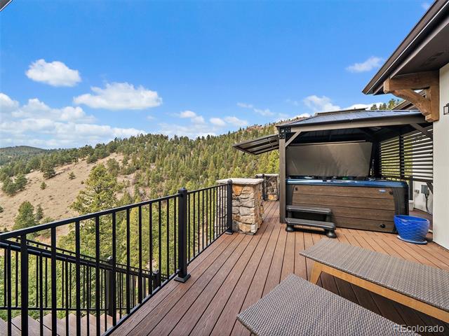 Elevated deck with a covered hot tub and lounge seating overlooking a forested mountain hillside.