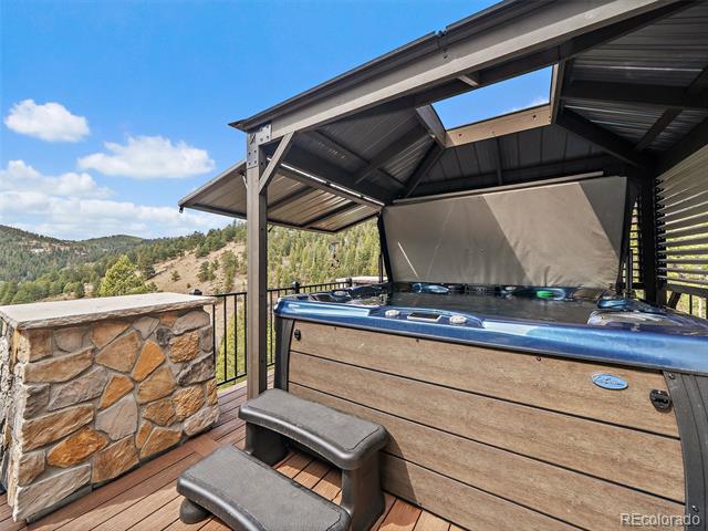 Covered deck hot tub with wooded mountain views and a stone half-wall.