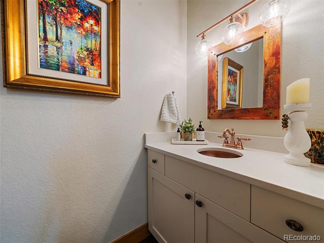 Bathroom vanity with a copper faucet, wood-framed mirror, and colorful framed artwork.