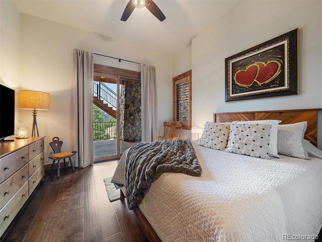 Bedroom with a wooden bed, gray throw, ceiling fan, and glass door opening to a balcony.