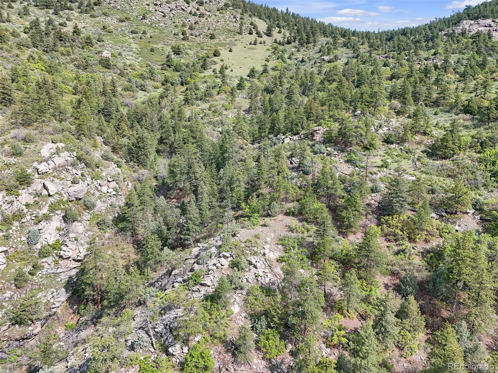 Aerial view of rocky, forested land with a grassy clearing among the hills.