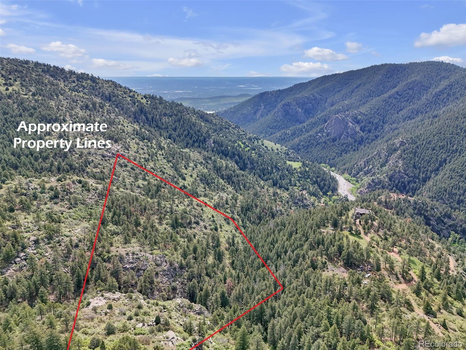 Aerial view of a wooded mountain parcel outlined in red, overlooking a forested valley and winding road.