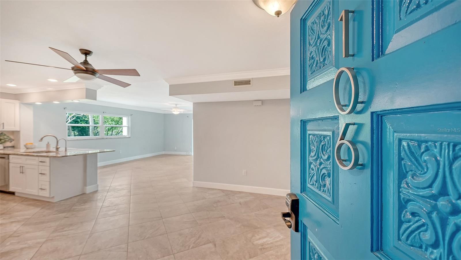 Open-plan condo interior with a white kitchen island and light tile floors, viewed through turquoise door 106.