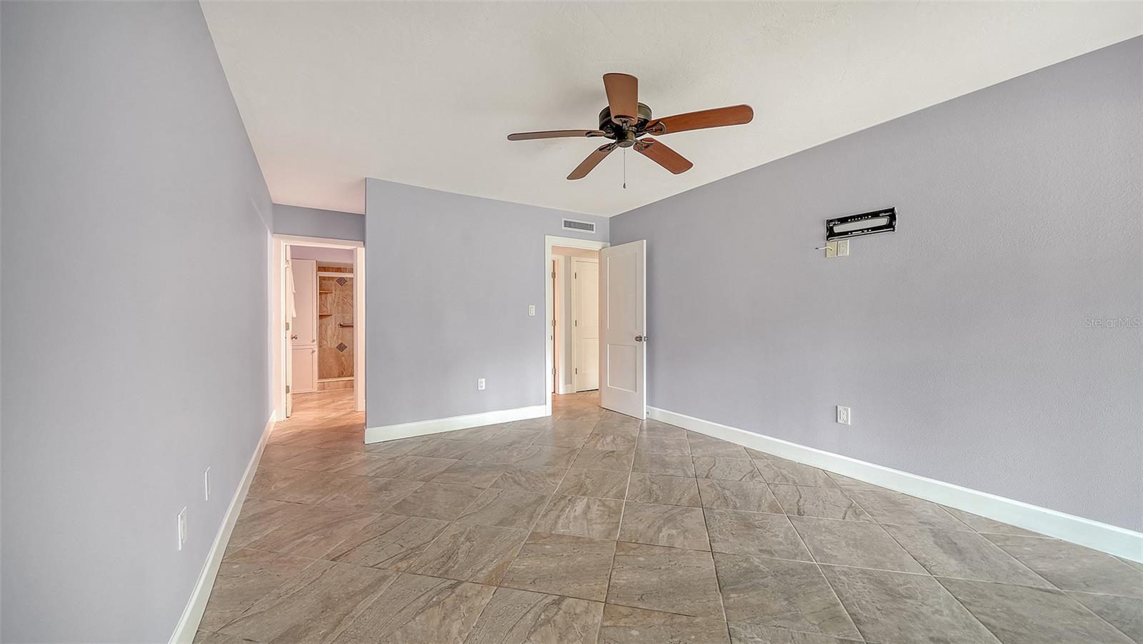 Vacant bedroom with beige tile flooring, gray walls, and a wood-blade ceiling fan.