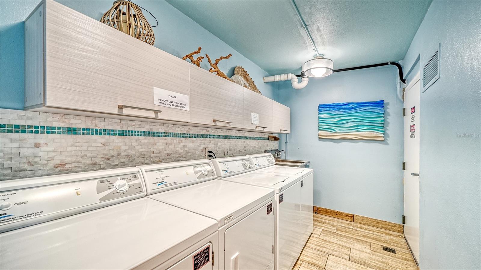 Laundry room with rows of white washers and dryers, pale cabinets, and colorful wave-shaped wall art.