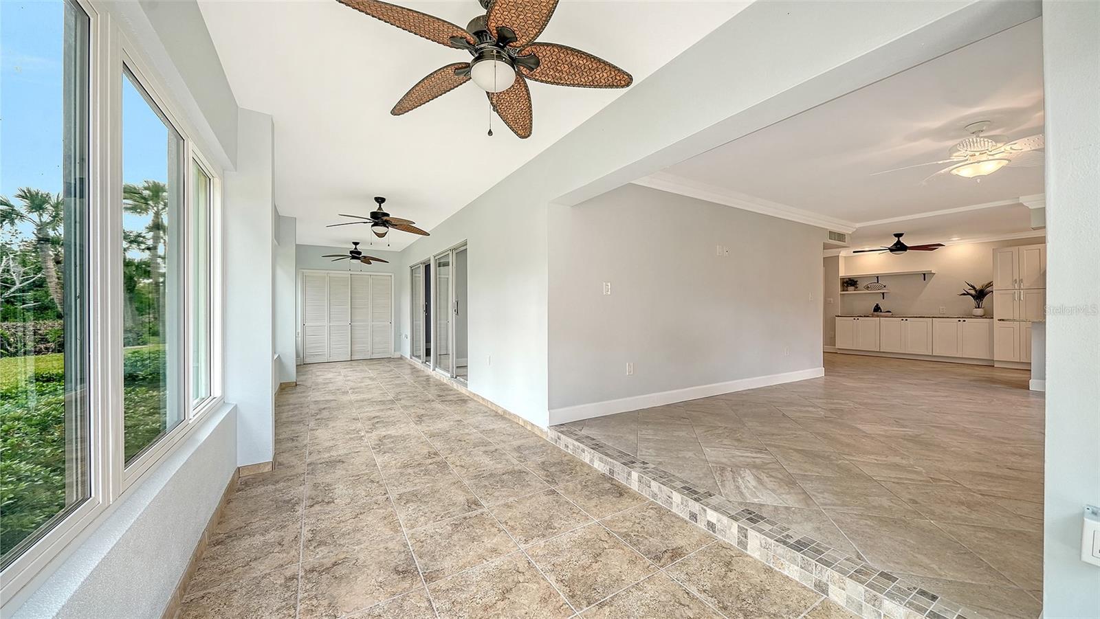Tiled sunroom with wide windows, ceiling fans, and an adjoining open living area and kitchen.
