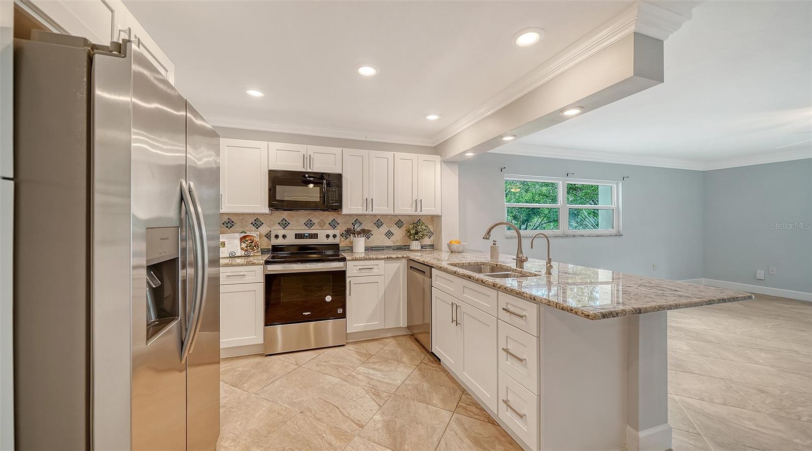Kitchen with white cabinets, stainless steel appliances, and a large granite island with double sink.