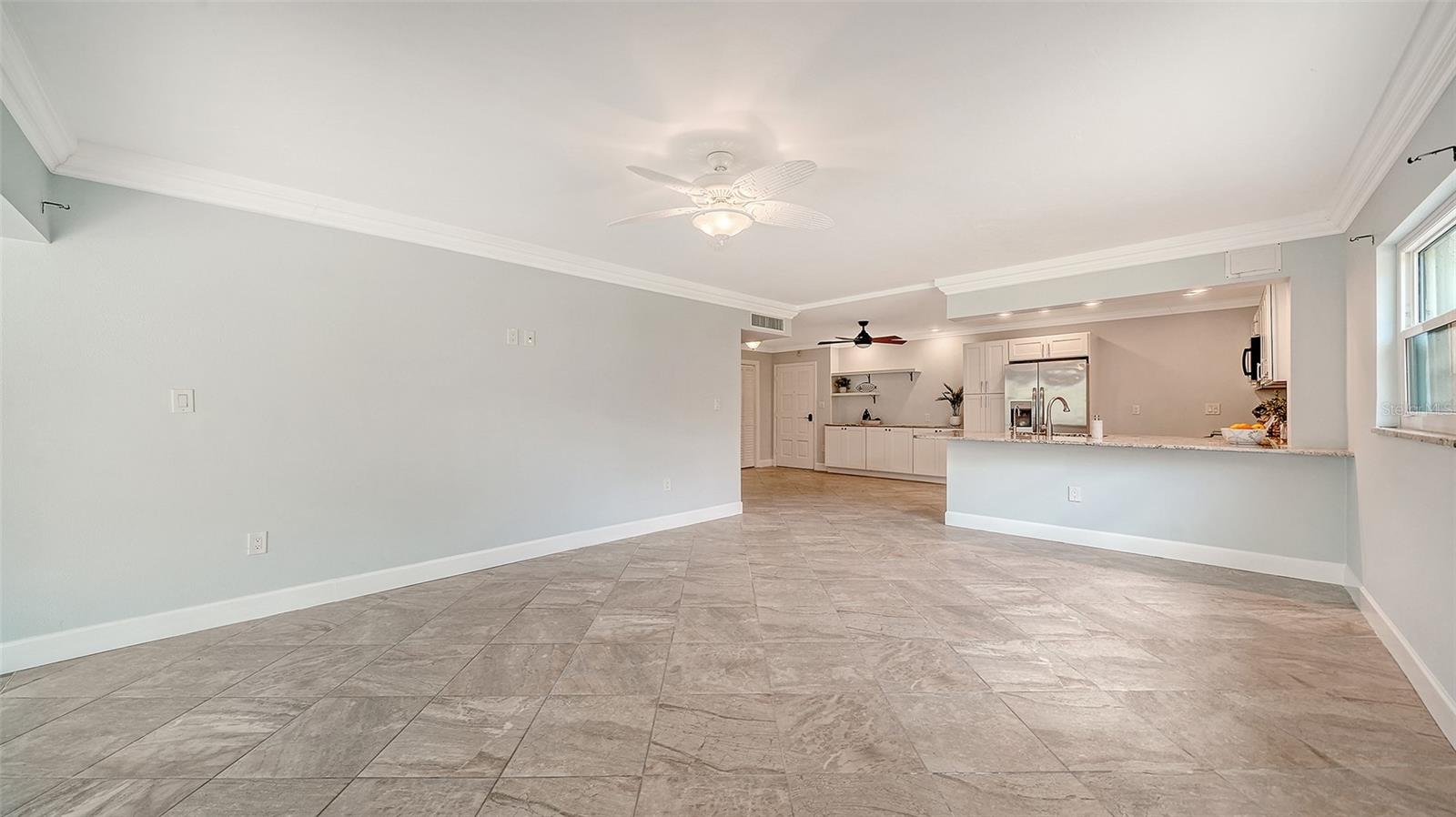 Open living area and kitchen with tile floors, a long breakfast bar, and stainless steel appliances.