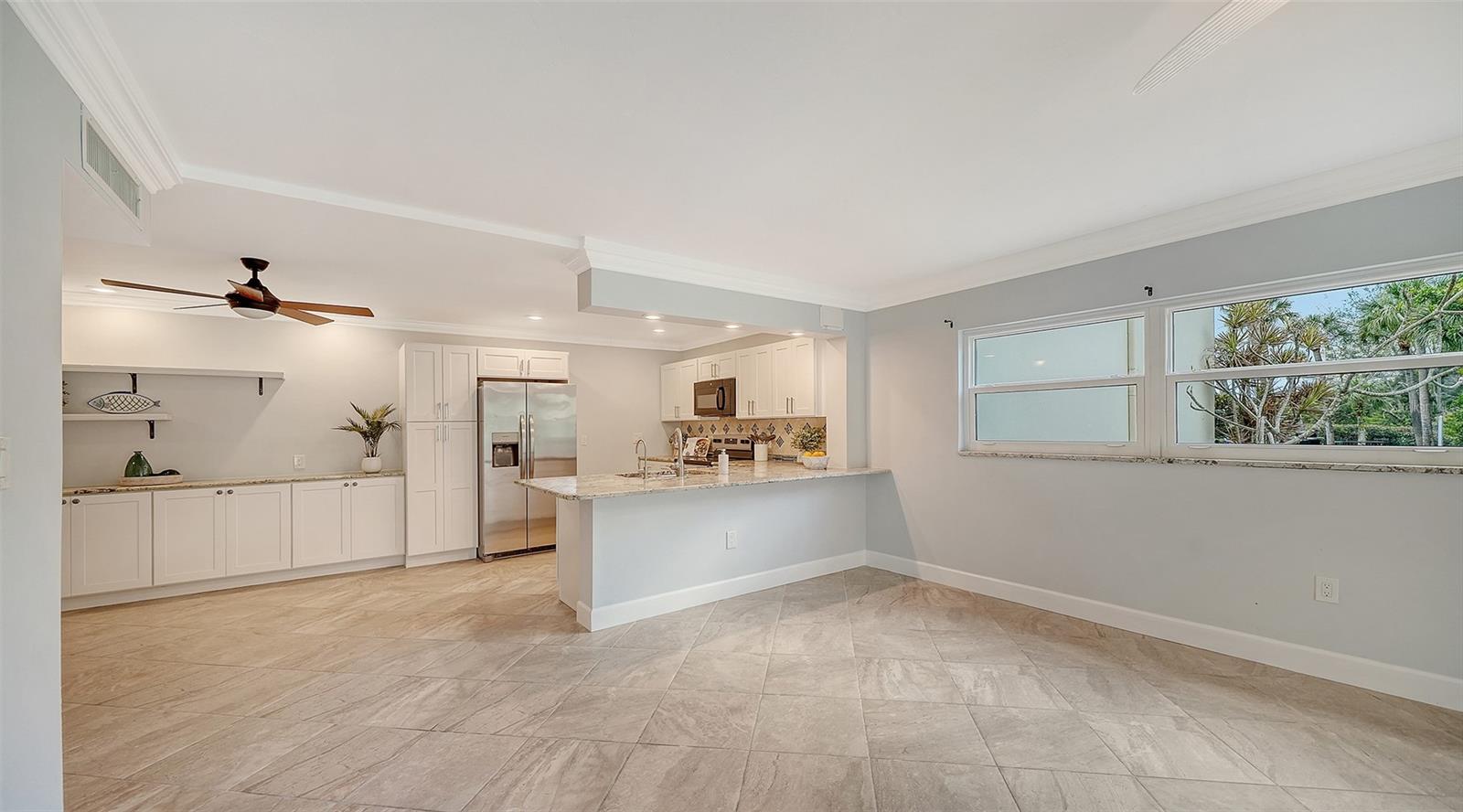 Open kitchen with white cabinets, stainless steel appliances, and a large peninsula beside wide windows.