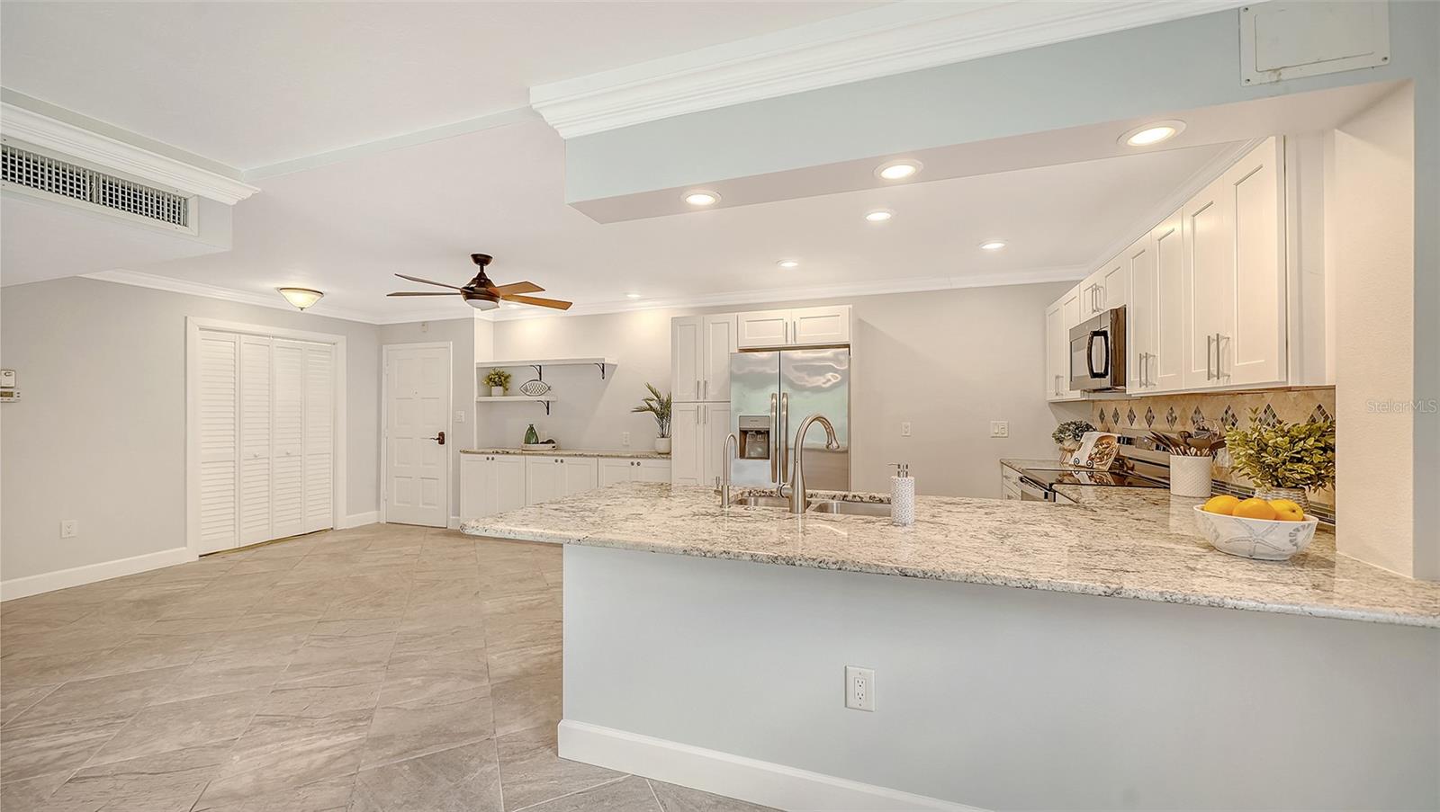 Open kitchen with white cabinets, stainless steel appliances, and a large granite island.