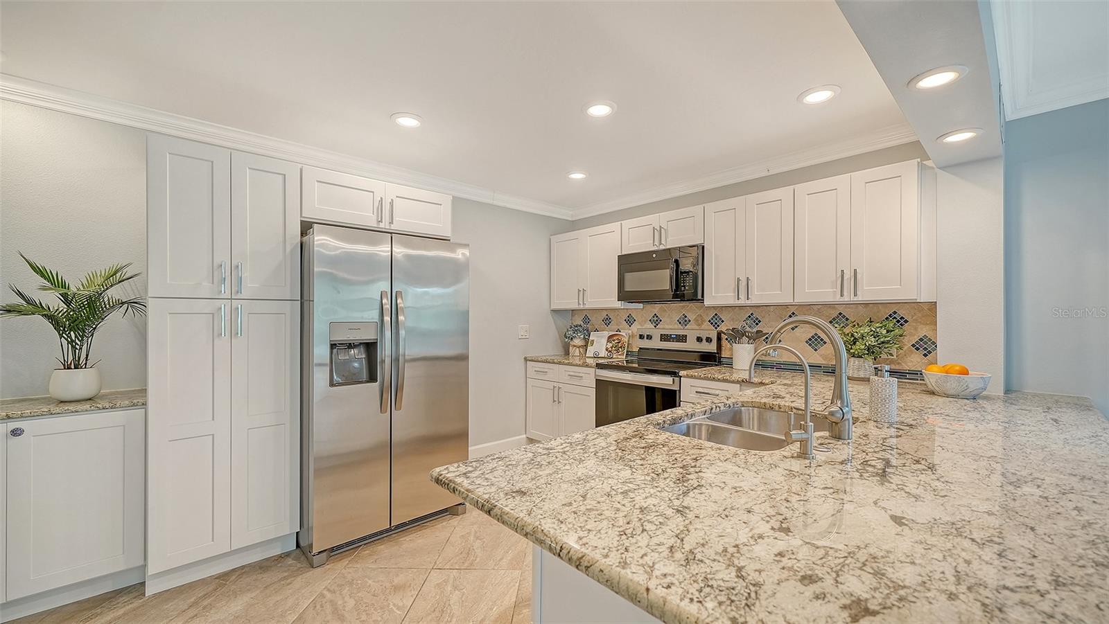 Kitchen with white cabinets, stainless steel appliances, patterned backsplash, and a large granite island.