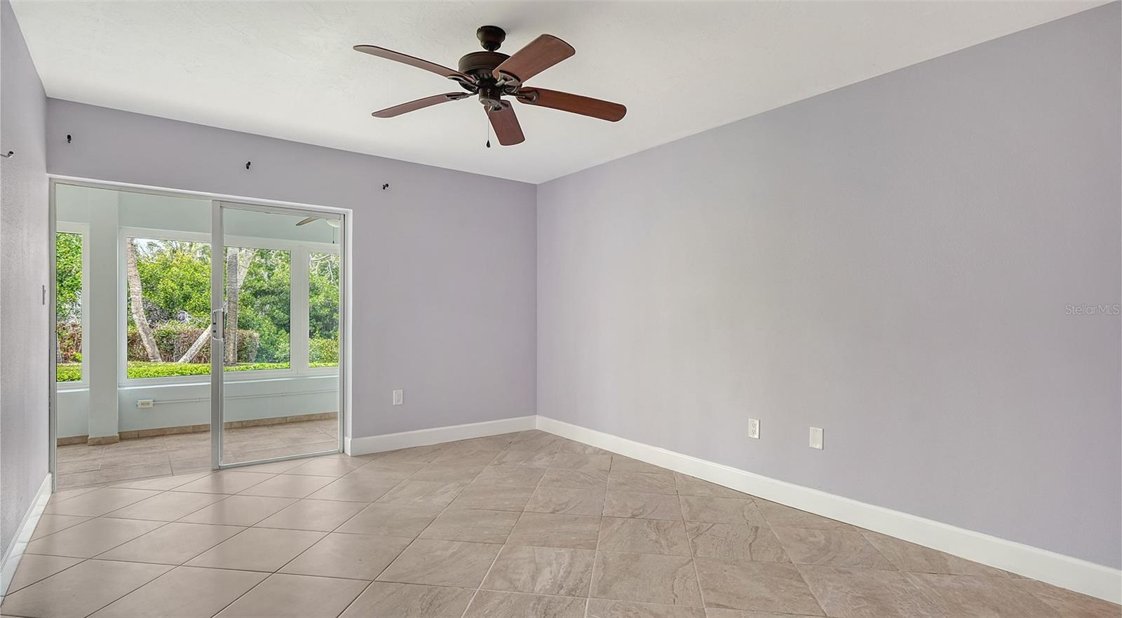 Empty tiled room with a ceiling fan and sliding glass door to a bright sunroom.
