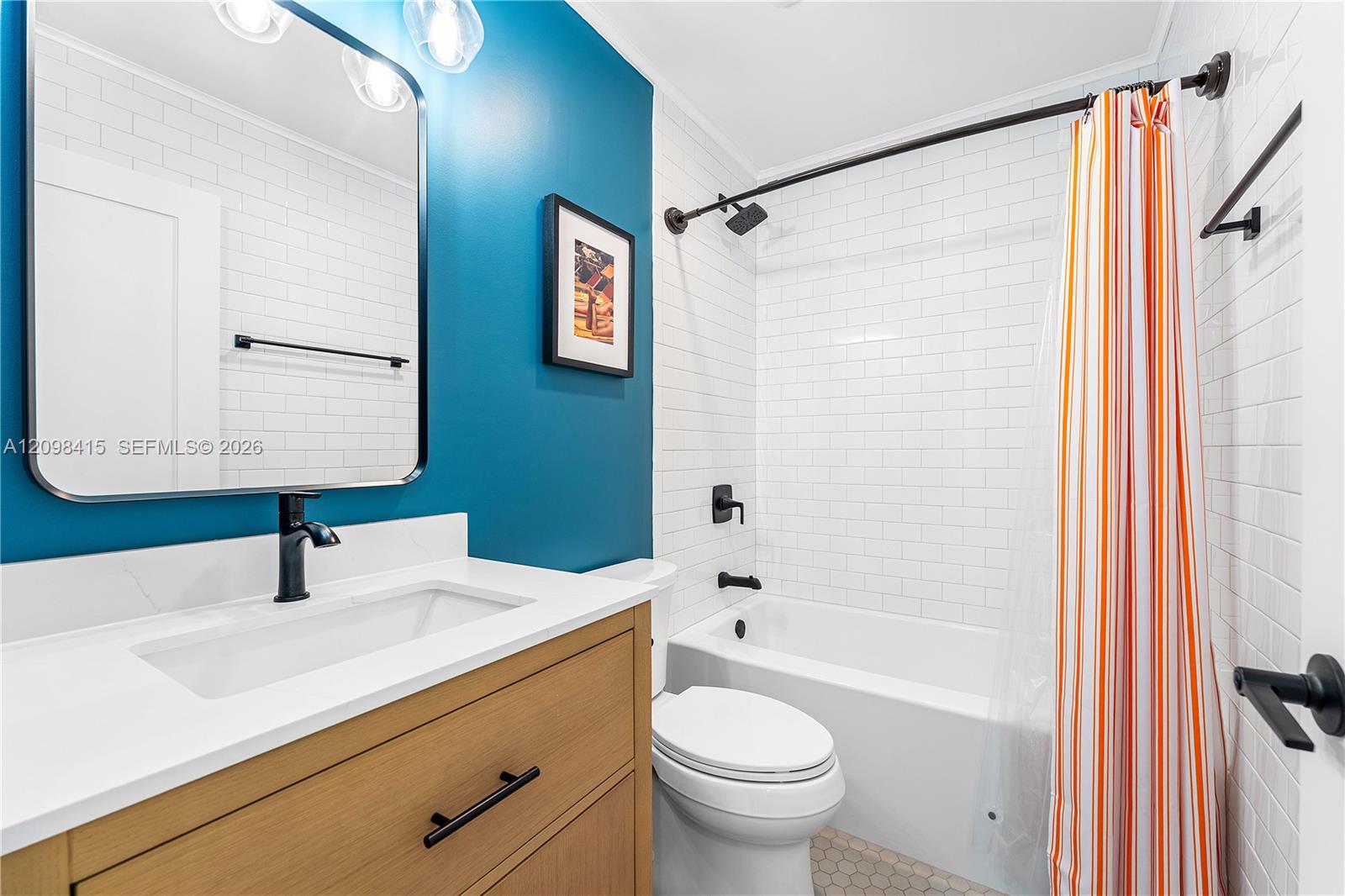 Bathroom with a wood vanity, teal accent wall, and white subway-tile tub behind a striped curtain.
