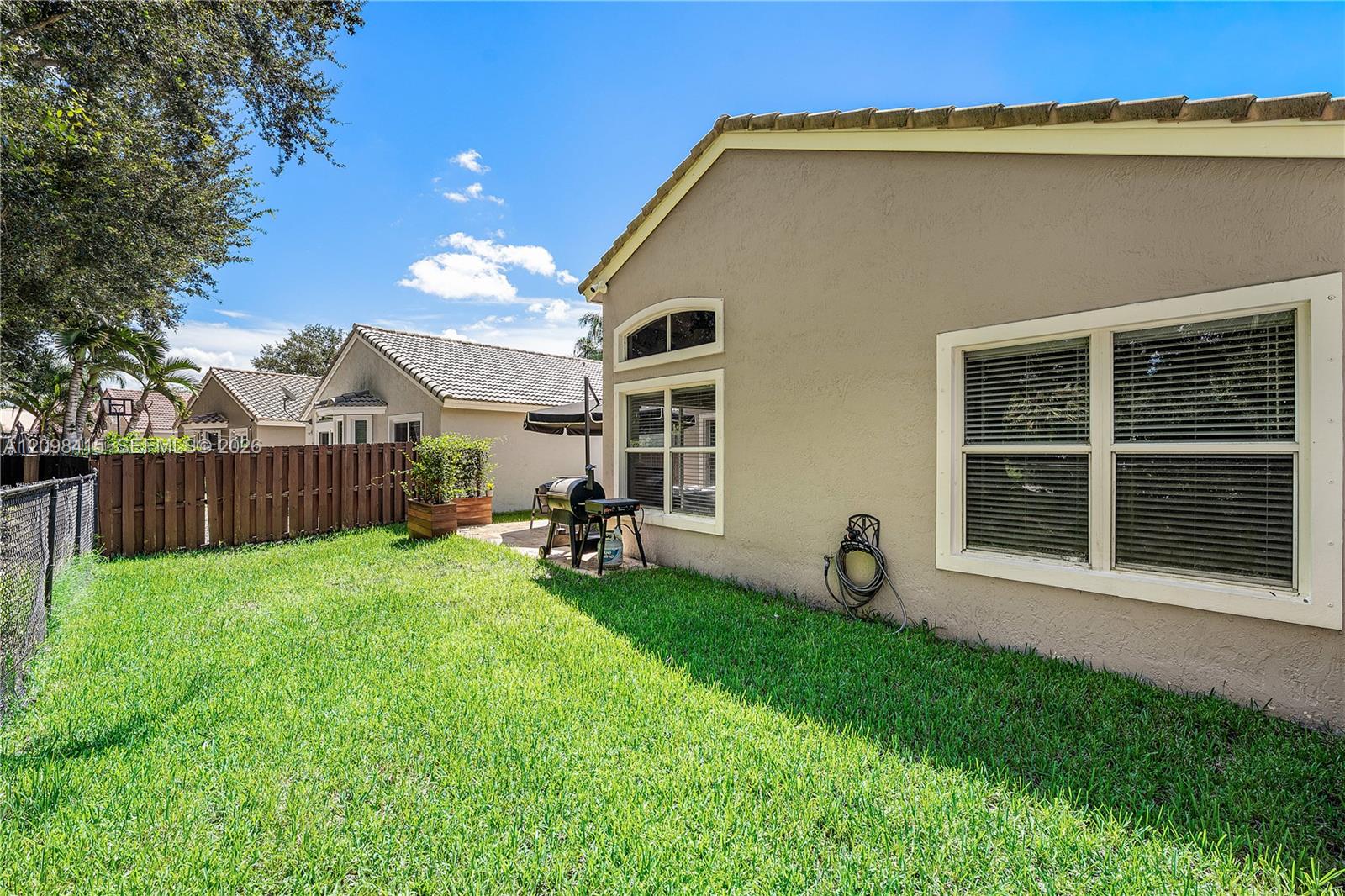 Home’s beige stucco rear exterior beside a fenced grassy backyard with a barbecue grill.