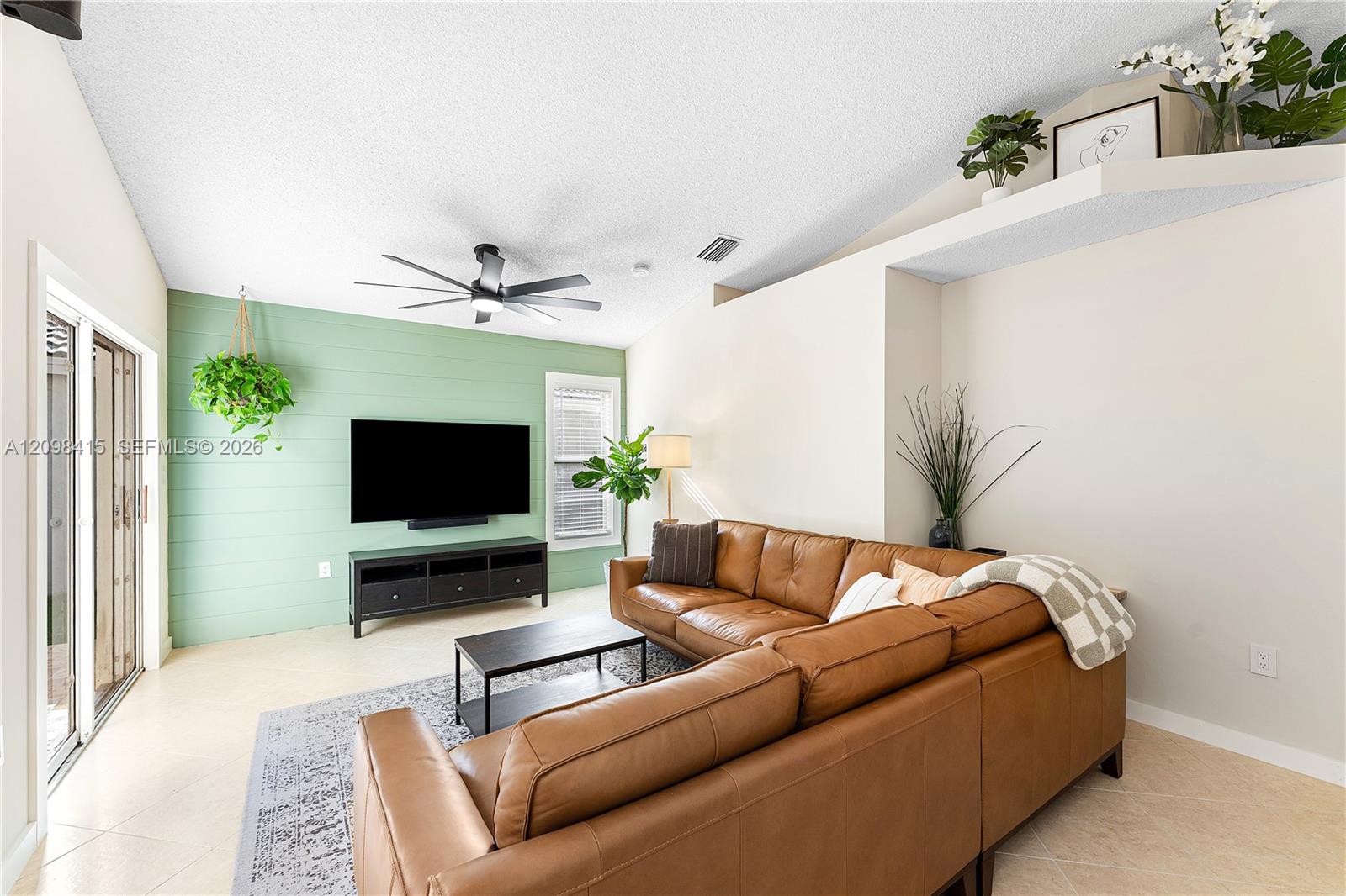 Living room with a brown leather sectional and TV against a mint-green paneled wall.