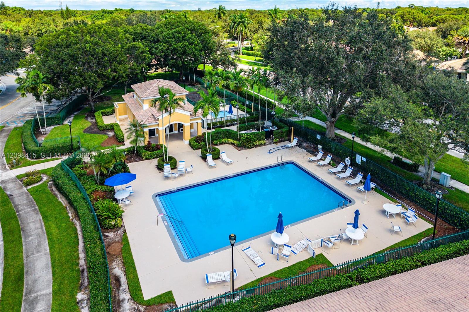 Aerial view of a community pool with a yellow-roofed building and palm trees.