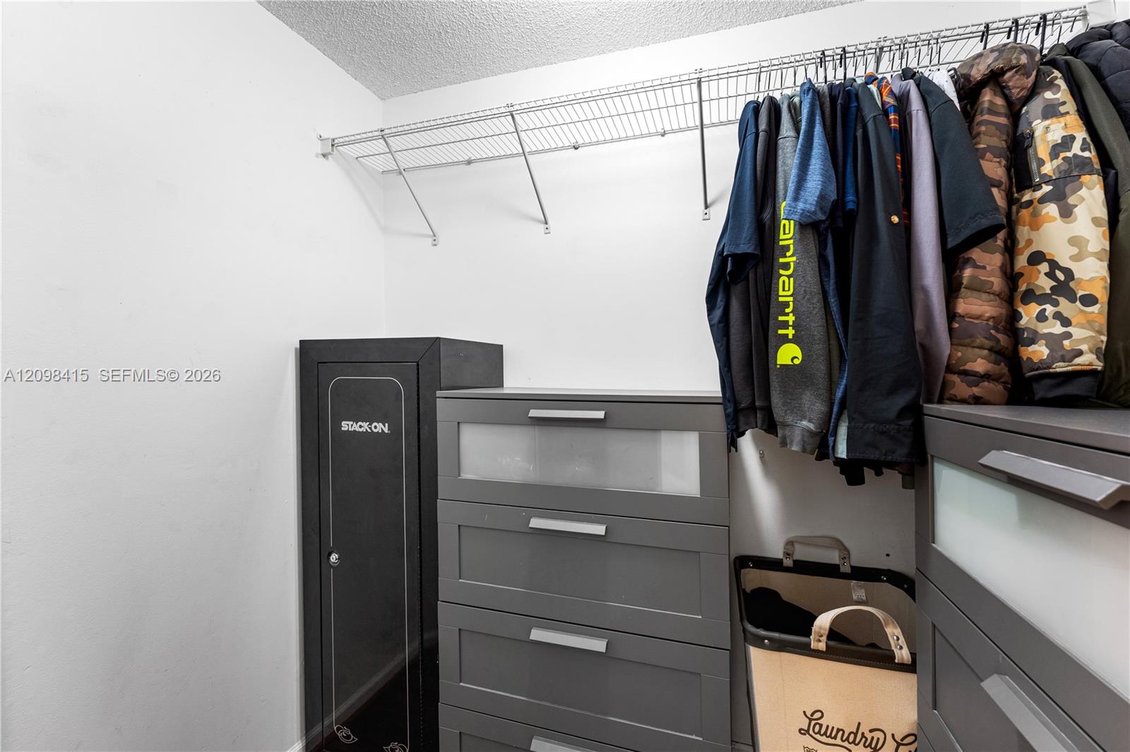 Walk-in closet with gray drawer units, hanging jackets, and a black safe.