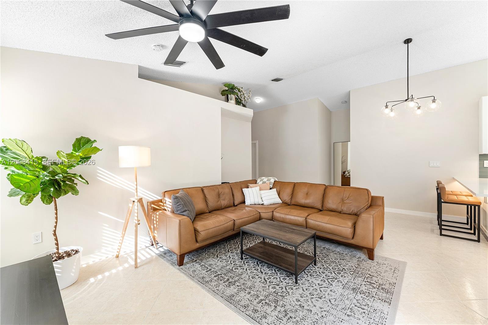 Living room with a tan leather sectional, patterned rug, and black ceiling fan.