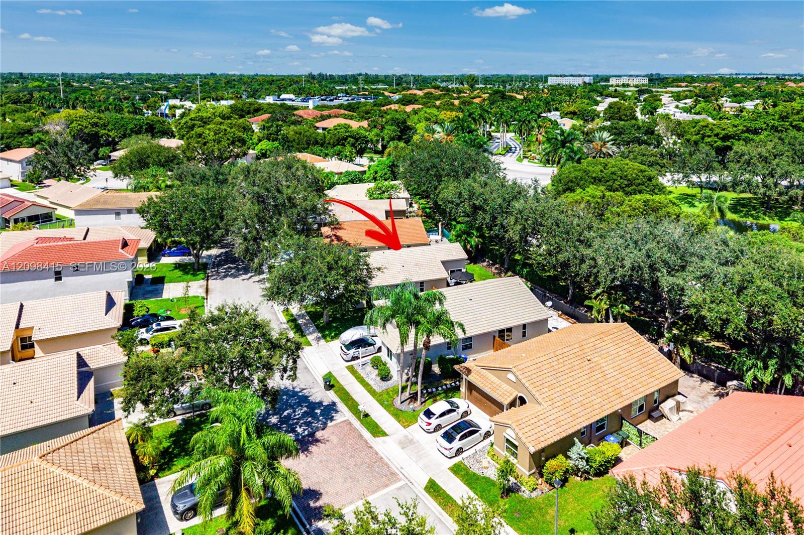 Aerial view of a single-story home marked by a red arrow among tropical, tile-roofed houses.