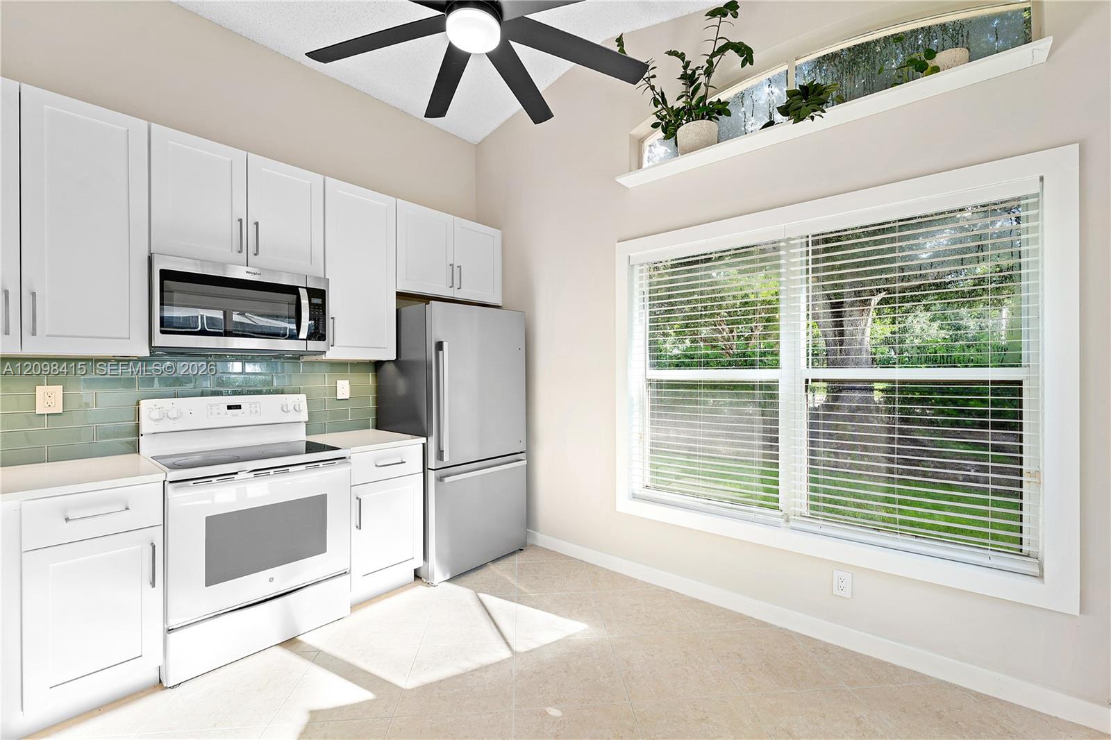 Bright kitchen with white cabinets, stainless appliances, pale green tile backsplash, and a large yard-facing window.