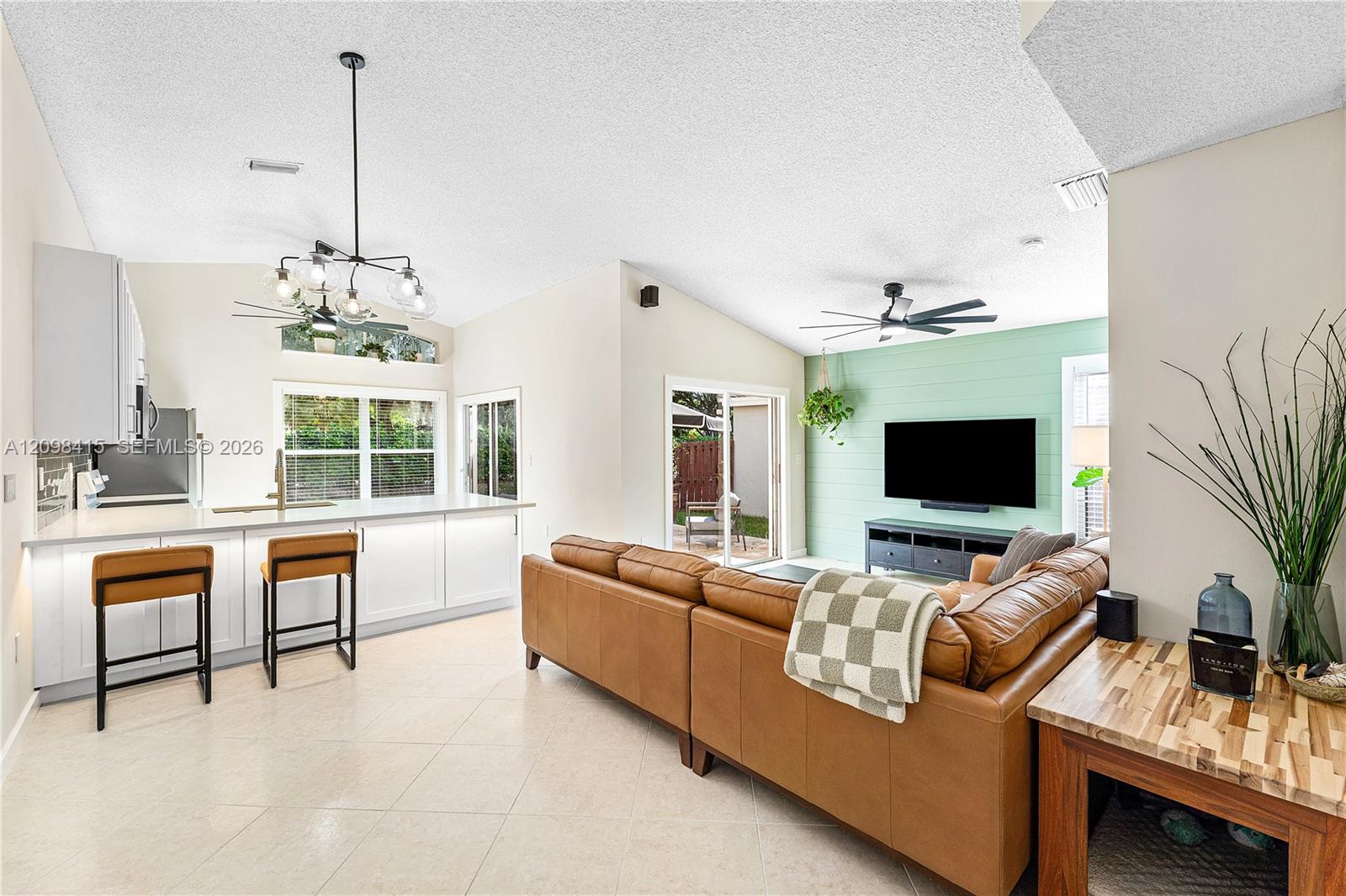 Open-plan kitchen and living room with a white island, caramel leather sectional, and mint-green TV wall.
