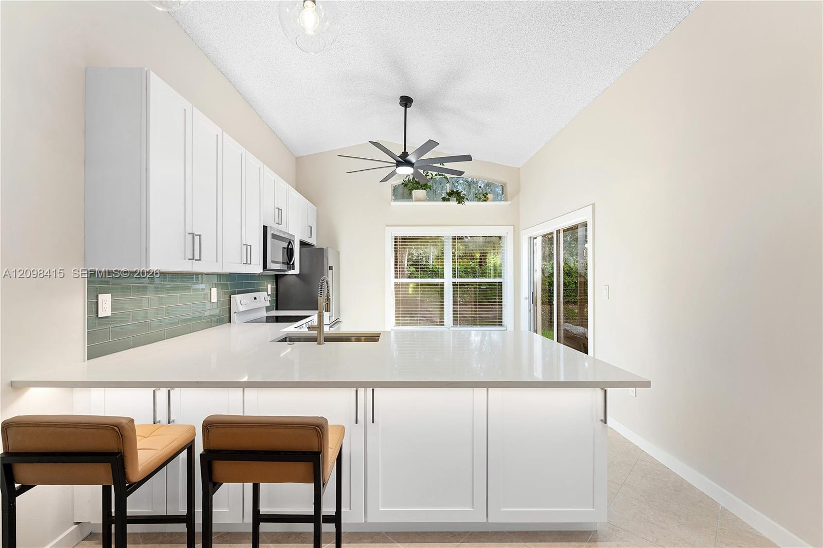 Bright kitchen with a white island, green tile backsplash, and vaulted ceiling.