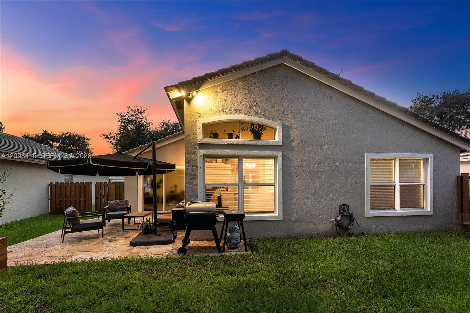 Gray stucco home with a furnished patio and grill at dusk.