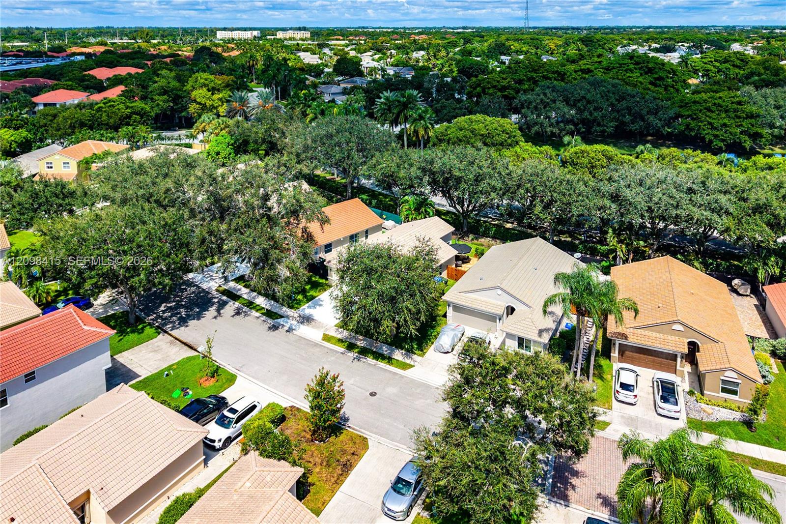 Aerial view of a leafy neighborhood with tiled-roof homes, palm trees, and tree-lined streets.
