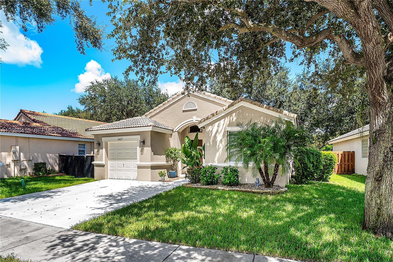 Single-story stucco home with a tiled roof, white garage door, palms, and a broad green lawn.