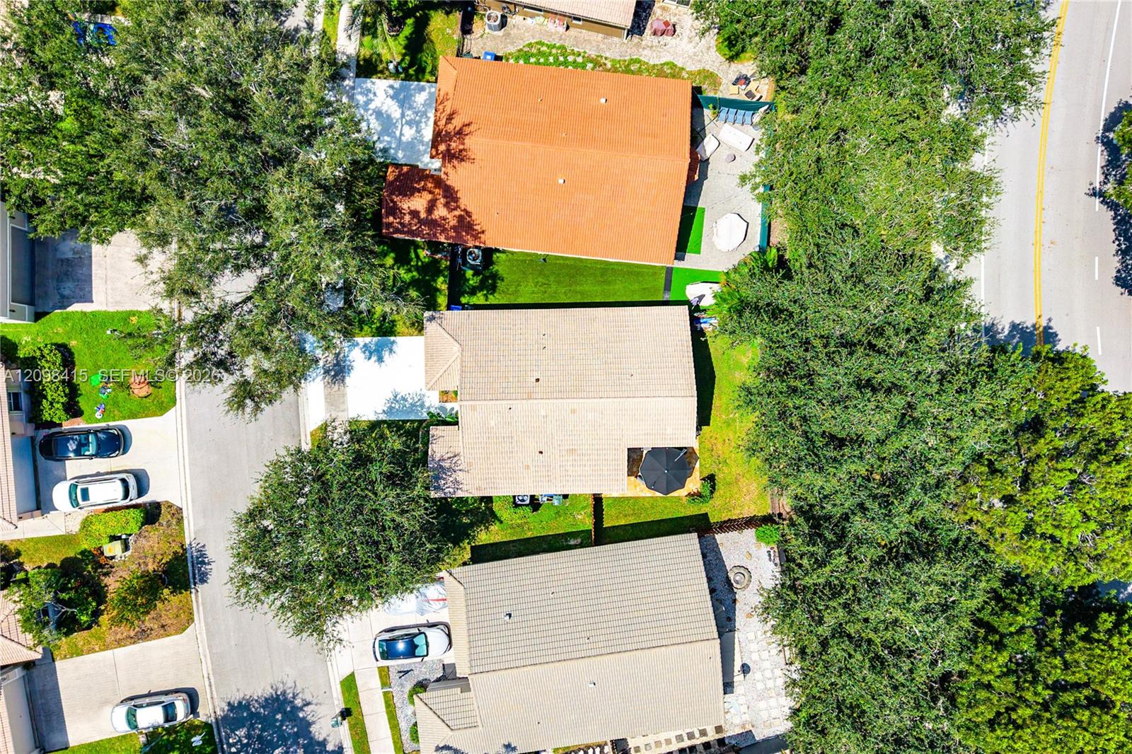 Aerial view of homes with tiled roofs and tree-shaded yards beside a residential road.