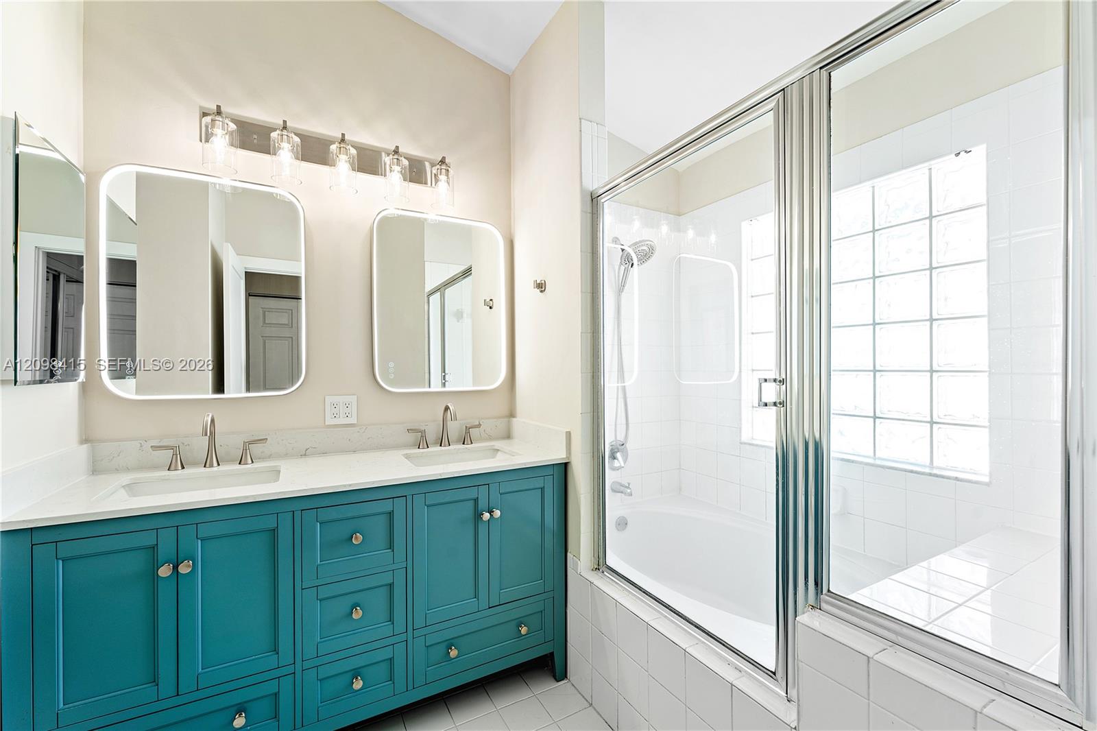 Bathroom with a teal double vanity and a glass-enclosed, white-tiled tub and shower.