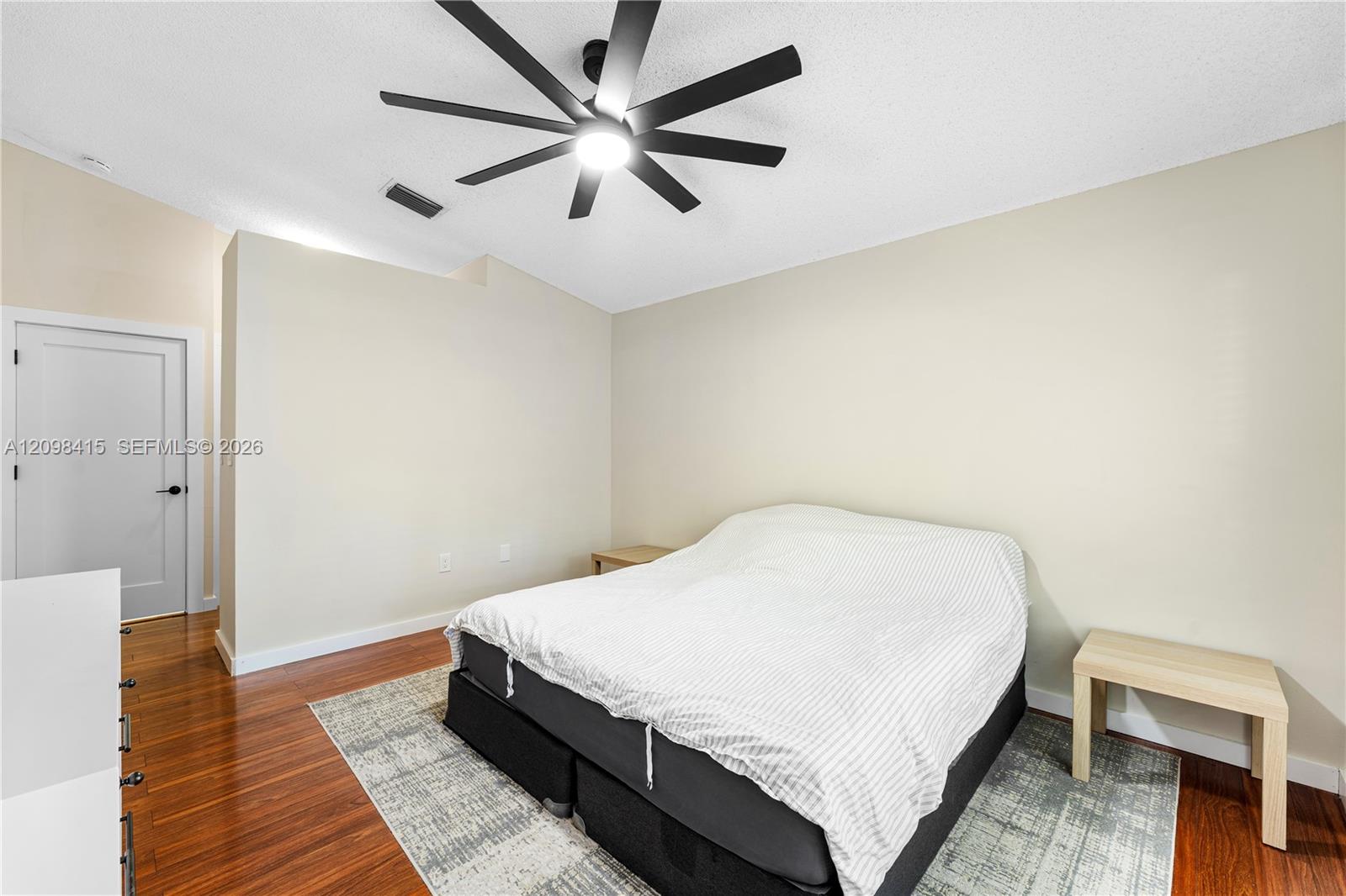 Bedroom with white striped bedding, wood flooring, a patterned rug, and a large black ceiling fan.
